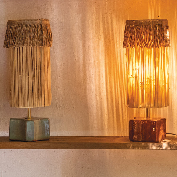 Lampes à poser, de chevet avec abat-jour en raphia et base en céramique artisanale, diffusant une lumière chaude et naturelle sur un mur texturé – création Honoré au style méditerranéen et authentique