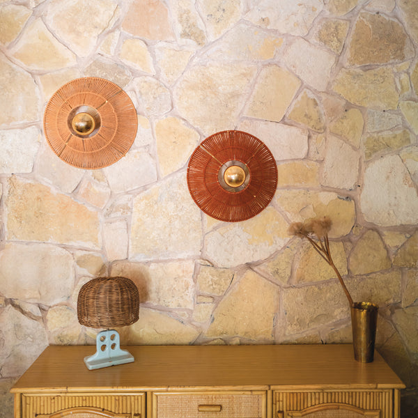 Appliques murales Virgo en laine tressée à la main, dans les coloris saumon et rouille, fixées sur un mur en pierre naturelle. Chaque applique est ornée d’un globe doré central, mêlant artisanat marocain et design contemporain dans une harmonie douce et lumineuse.