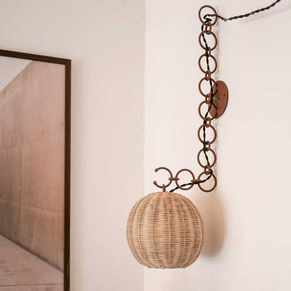 Appliques murales en rotin suspendues à des chaînes décoratives en métal. ambiance naturelle et artisanale avec des matières brutes et des détails faits main, typiques du style méditerranéen d’intérieur.
