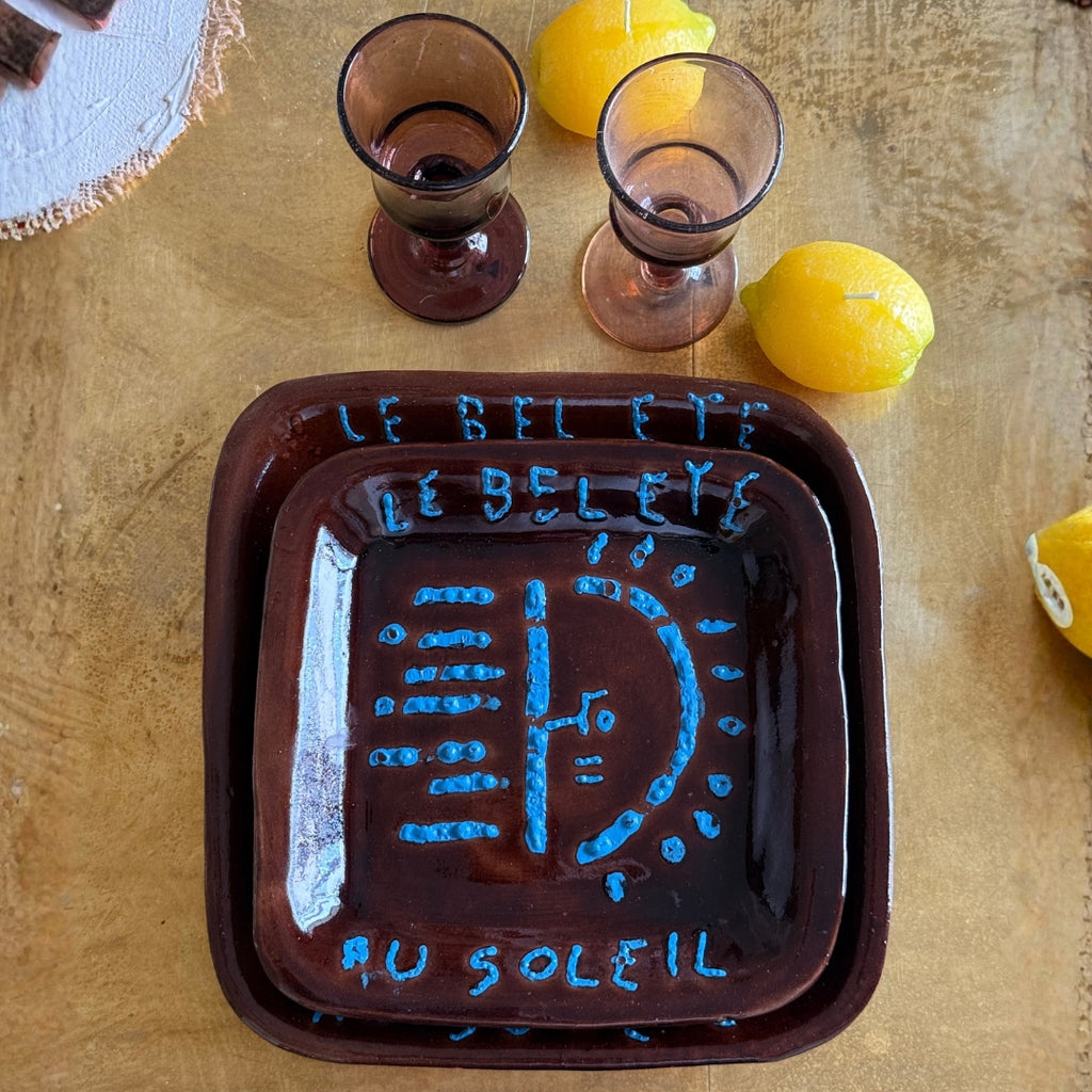 Composition artistique de vaisselle artisanale avec assiettes décoratives, verres teintés et pichet sur fond jaune inspiré du sud de la France