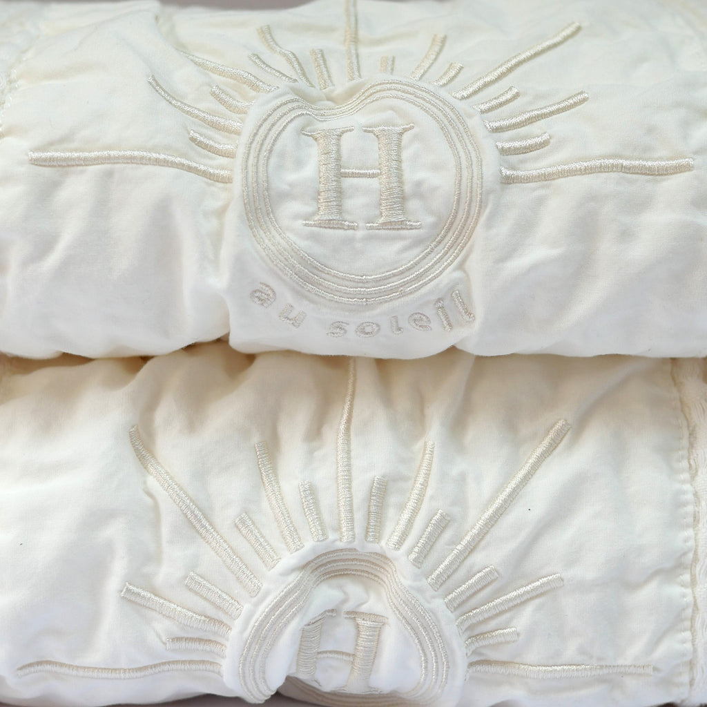 Serviettes de bain gaufrées en coton nid d’abeille couleur écru, avec detail broderie emblématique Honoré en forme de soleil, empilées avec élégance linge de bain doux et raffiné.