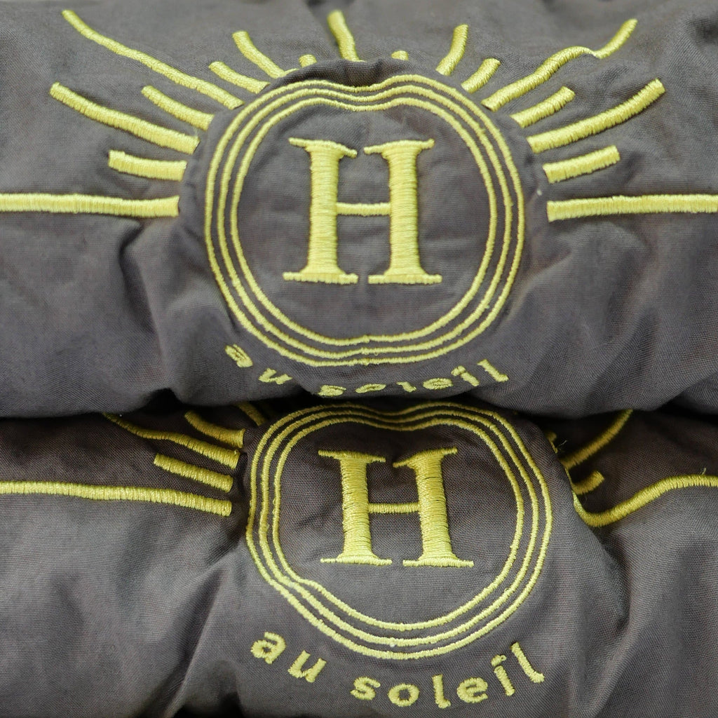 Détail serviettes gaufrées en coton nid d’abeille gris foncé, brodées du logo soleil Honoré. Linge de bain élégant et absorbant, au style artisanal.