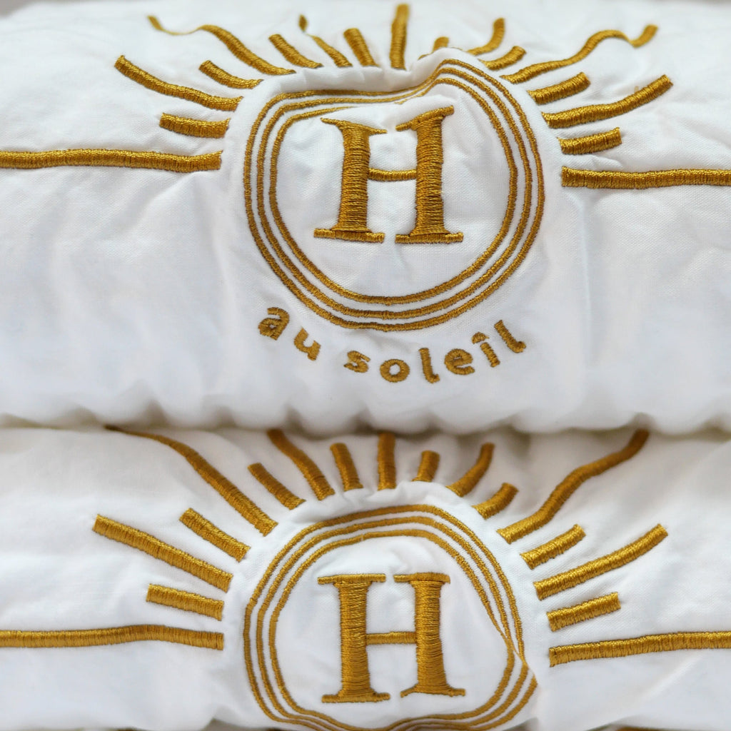 détail serviettes gaufrées en coton nid d’abeille blanc ornées de broderies soleil signées Honoré. Taille 50x100 80x160 