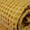 Détail serviettes gaufrées en coton nid d’abeille couleur jaune, avec broderie emblématique Honoré en forme de soleil, empilées avec élégance – linge de bain doux et raffiné.