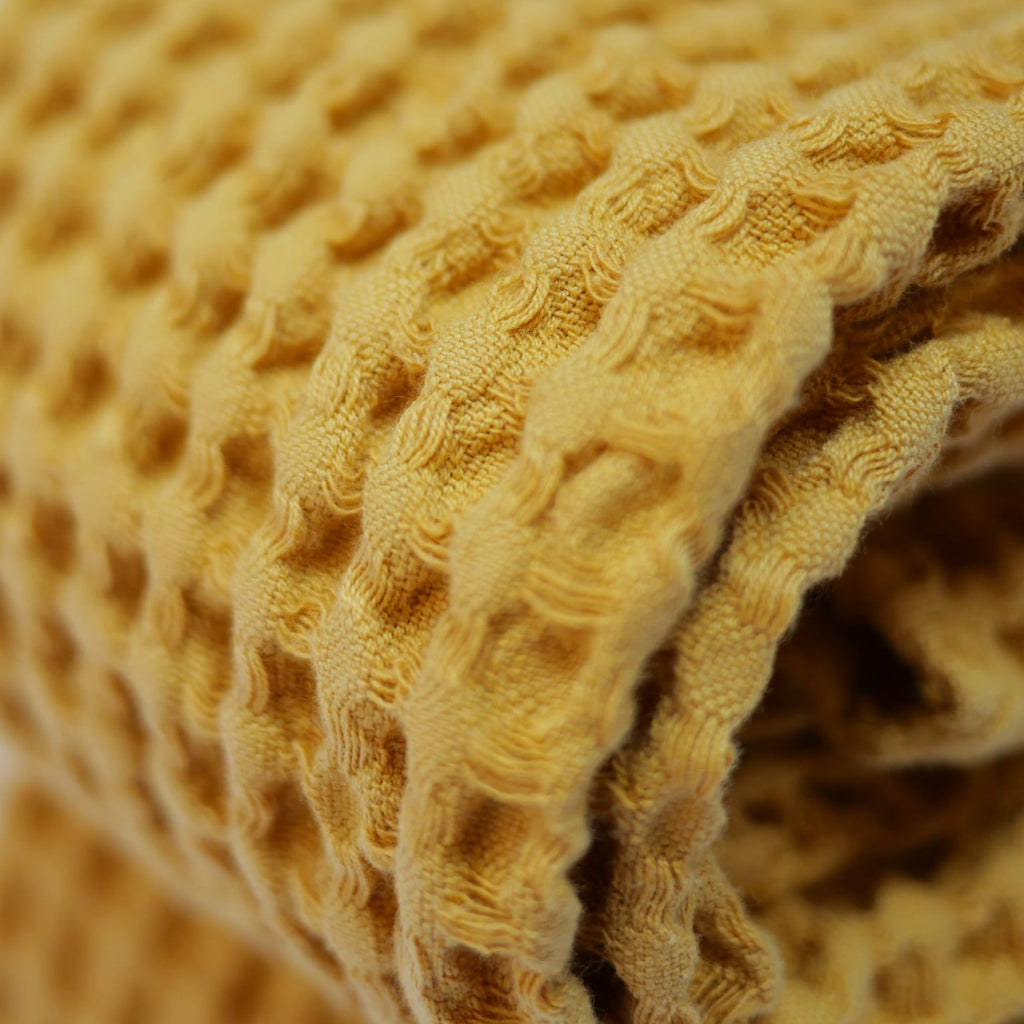 Détail serviettes gaufrées en coton nid d’abeille couleur jaune, avec broderie emblématique Honoré en forme de soleil, empilées avec élégance – linge de bain doux et raffiné.