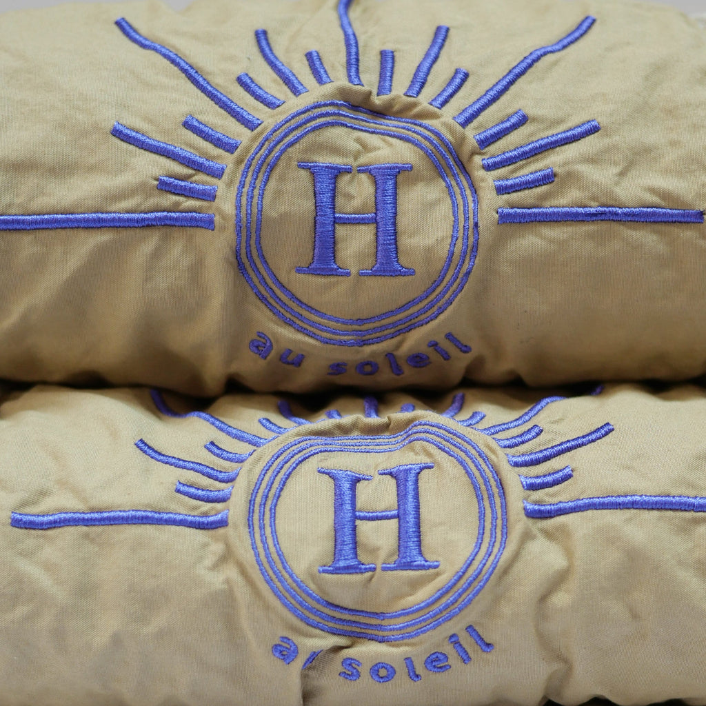 Ensemble de serviettes gaufrées en coton nid d’abeille couleur beige, avec detail broderie violet emblématique Honoré en forme de soleil, empilées avec élégance linge de bain doux et raffiné taille 50X100 80X160