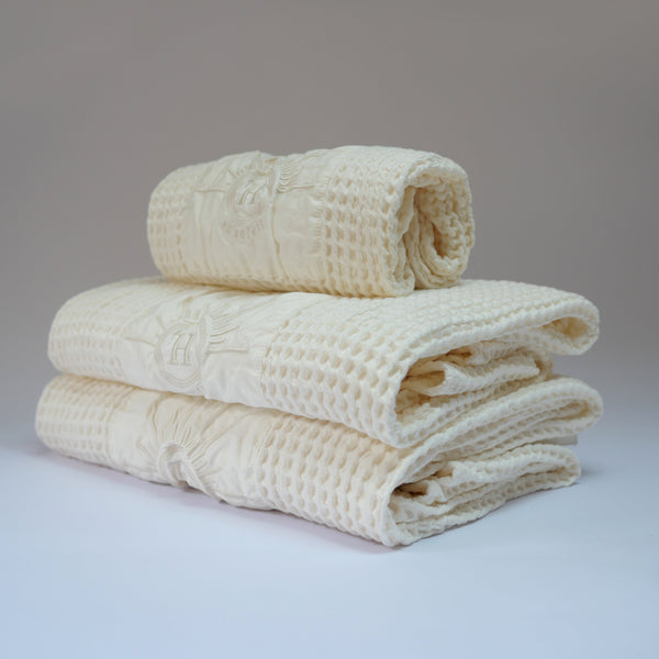 Ensemble de serviettes de bain gaufrées en coton nid d’abeille couleur écru, avec broderie emblématique Honoré en forme de soleil, empilées avec élégance, linge de bain doux et raffiné
