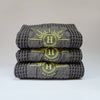 Ensemble de serviettes gaufrées en coton nid d’abeille couleur gris beton, avec broderie emblématique Honoré en forme de soleil, empilées avec élégance linge de bain doux et raffiné. 50 x 100 ou 80 x 160