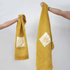 Serviettes gaufrées en coton nid d’abeille jaune, brodées du logo soleil Honoré, tenues à la main – linge de bain élégant et absorbant, au style artisanal.