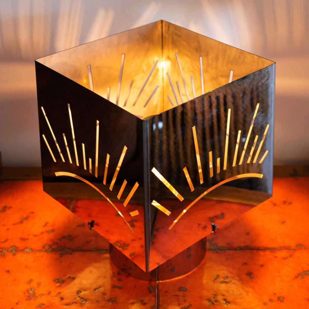 Lampe à poser design en métal inox découpé motif soleil, diffusant une lumière chaleureuse sur table en bois — luminaire décoratif artisanal Honoré.