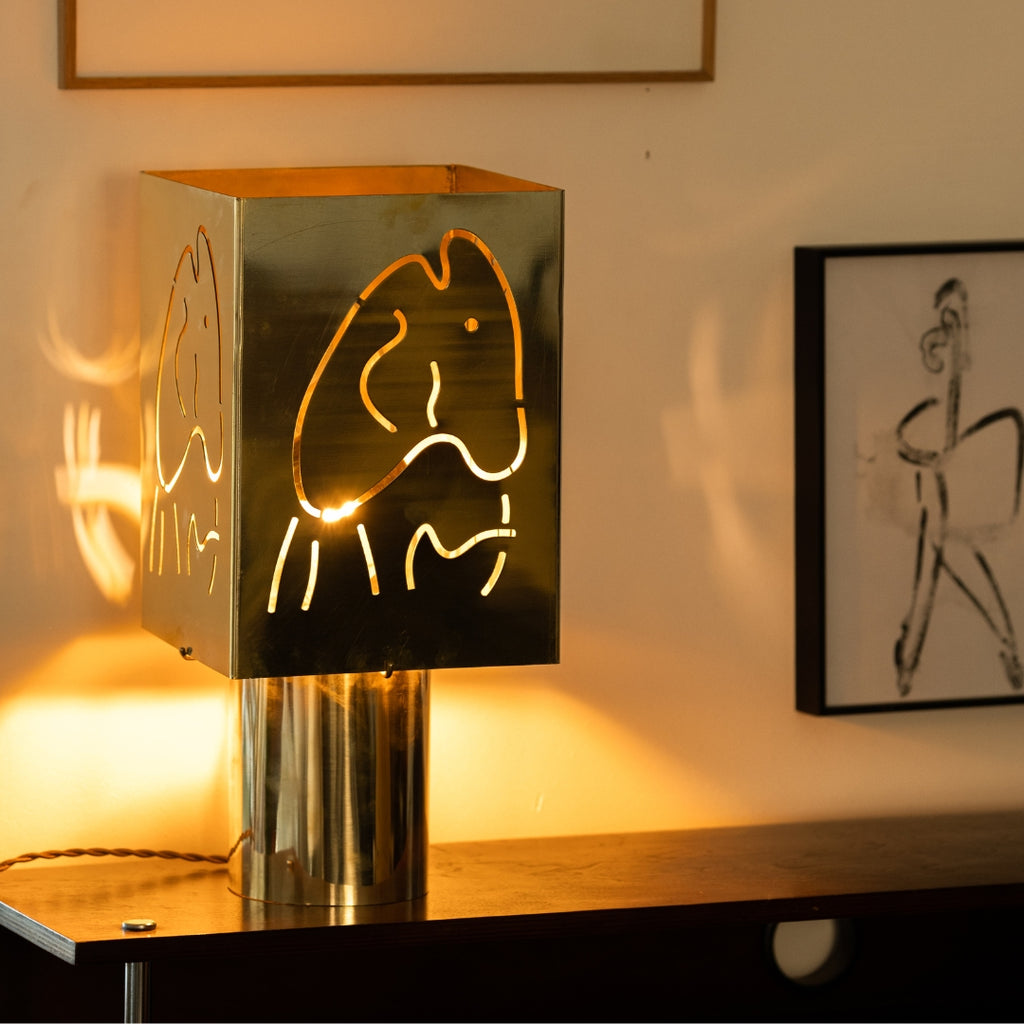 Lampe à poser design en métal chrome inox découpé motif poisson diffusant une lumière chaleureuse sur table en bois — luminaire décoratif artisanal Honoré.