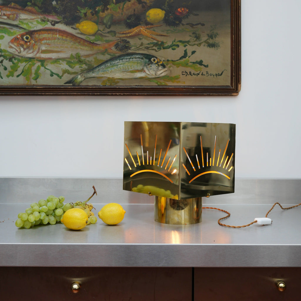 Lampe à poser design en métal inox laiton découpé motif soleil, diffusant une lumière chaleureuse sur table en bois — luminaire décoratif artisanal Honoré.