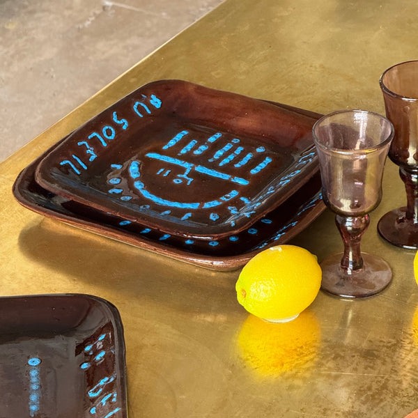Décor de table artistique avec céramiques peintes à la main, verres fumés et éléments naturels évoquant une atmosphère provençale