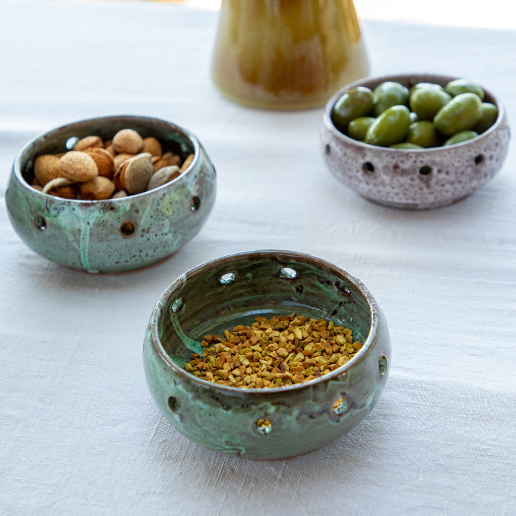 ramequin vert texturé trou en céramique lanzarote sur table nappe blanche avec pistache olive et noix