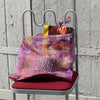 Sac tote bag en organza imprimé tartan transparent, décoré de broderies colorées inspirées de Marseille — le soleil, la mer, la Bonne Mère et les poissons. Posé sur une chaise en métal à assise bordeaux, ce sac léger et artistique incarne l’esprit ensoleillé et méditerranéen d’Honoré.