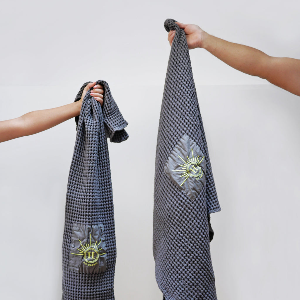 Serviettes gaufrées en coton nid d’abeille gris foncé, brodées du logo soleil Honoré, tenues à la main, linge de bain élégant et absorbant, au style artisanal