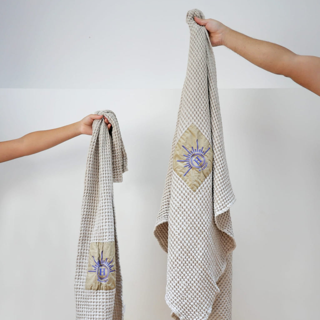 Serviettes de bain gaufrées en coton nid d’abeille bronze, brodées du logo soleil Honoré, tenues à la main  linge de bain élégant et absorbant, au style artisanal