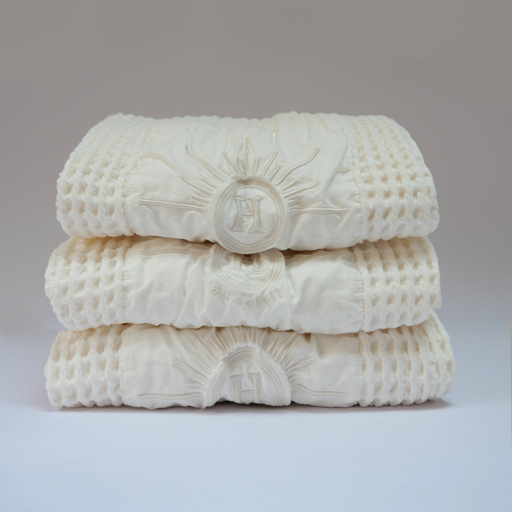 Serviettes gaufrées en coton nid d’abeille blanc ecru, brodées du logo soleil Honoré, tenues à la main linge de bain élégant et absorbant, au style artisanal