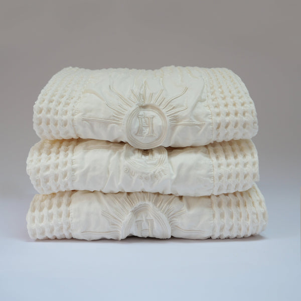 Serviettes gaufrées en coton nid d’abeille blanc ecru, brodées du logo soleil Honoré, tenues à la main linge de bain élégant et absorbant, au style artisanal