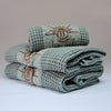 Ensemble de serviettes de bain profil gaufrées en coton nid d’abeille couleur bleu céladon, avec broderie bronze emblématique Honoré en forme de soleil, empilées : linge de bain doux et raffiné taille 50x100 80x160