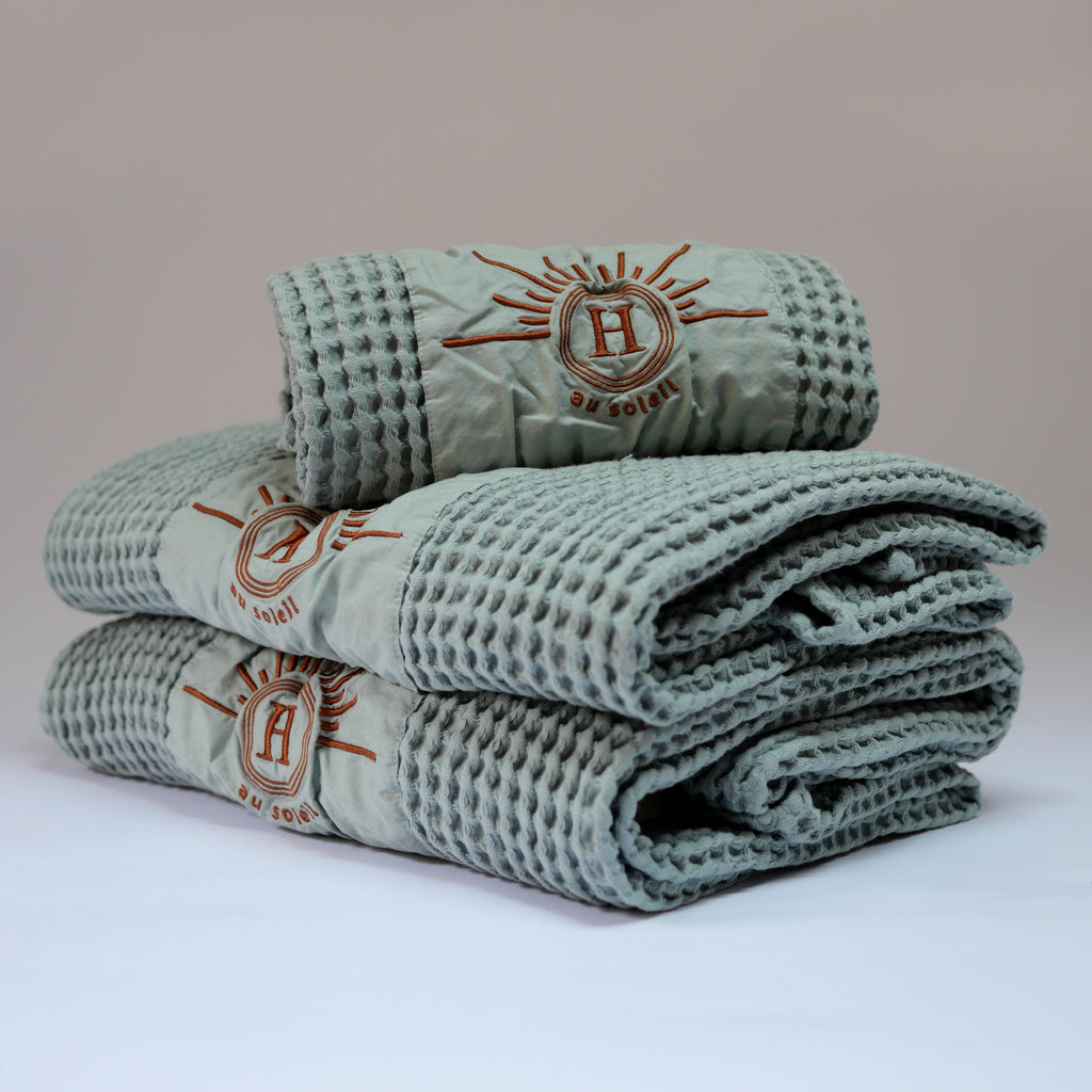 Ensemble de serviettes de bain profil gaufrées en coton nid d’abeille couleur bleu céladon, avec broderie bronze emblématique Honoré en forme de soleil, empilées : linge de bain doux et raffiné taille 50x100 80x160
