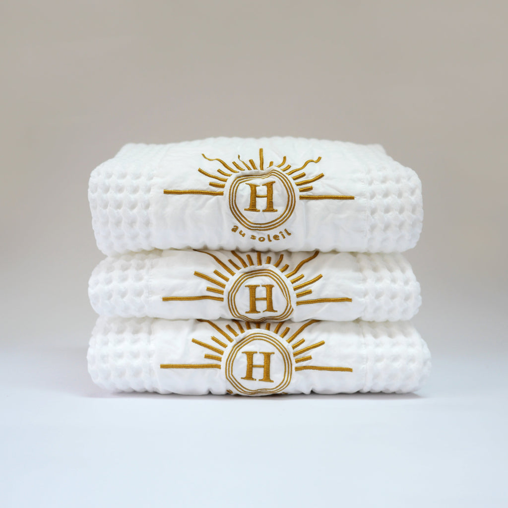 Collection de serviettes gaufrées en coton nid d’abeille blanc ornées de broderies soleil signées Honoré. Taille 50x100 80x160 