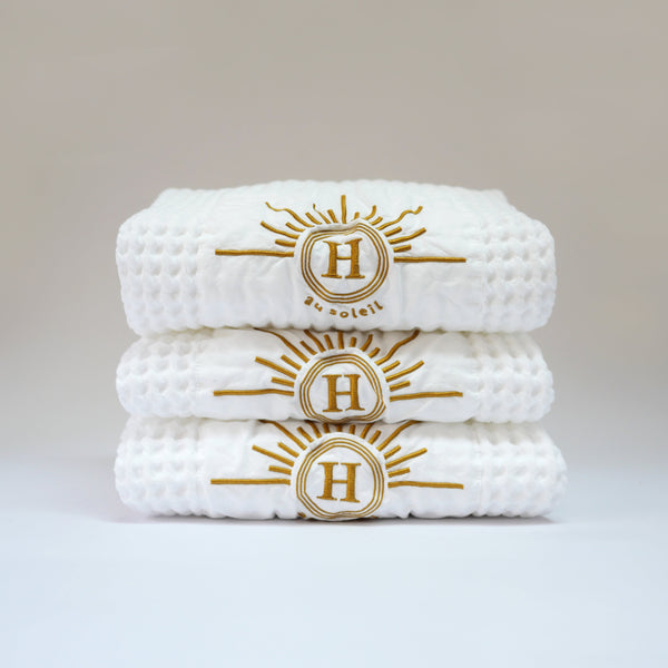 Collection de serviettes gaufrées en coton nid d’abeille blanc ornées de broderies soleil signées Honoré. Taille 50x100 80x160 