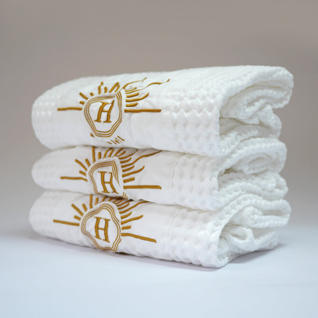 Ensemble de serviettes gaufrées en coton nid d’abeille blanc ornées de broderies soleil signées Honoré de profil. Taille 50x100 80x160 