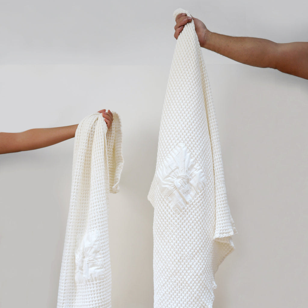 Serviettes gaufrées en coton nid d’abeille ecru, brodées du logo soleil Honoré, tenues à la main linge de bain élégant et absorbant, au style artisanal.