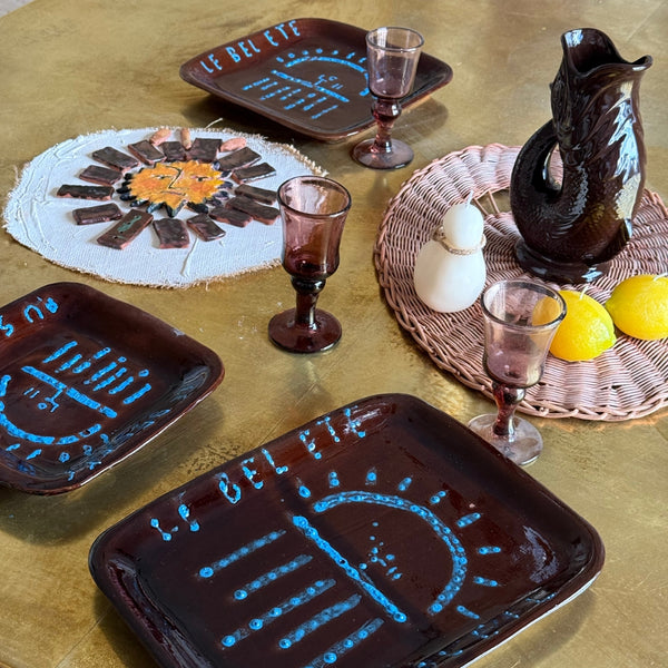 Nature morte méditerranéenne avec assiettes en céramique artisanale marron décorées de motifs soleil bleus sur table jaune texturée