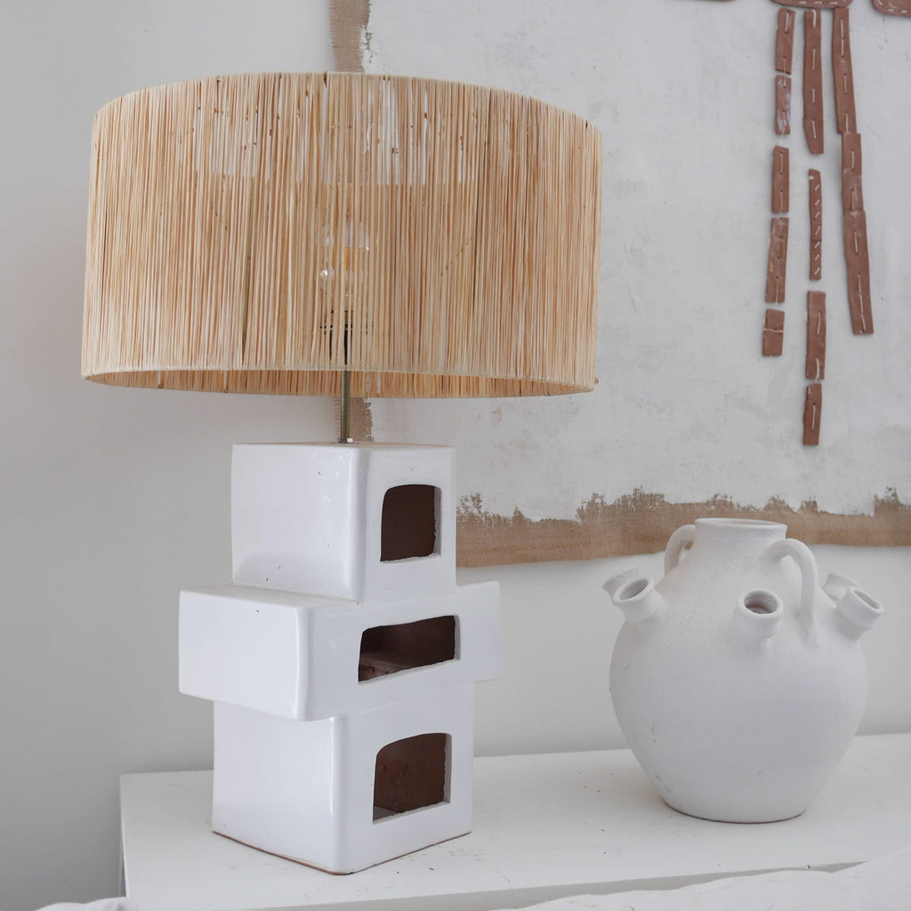 Lampe à poser en céramique artisanale blanc, forme géométrique sculpturale avec abat-jour en raphia naturel — luminaire design pour salon ou chambre.